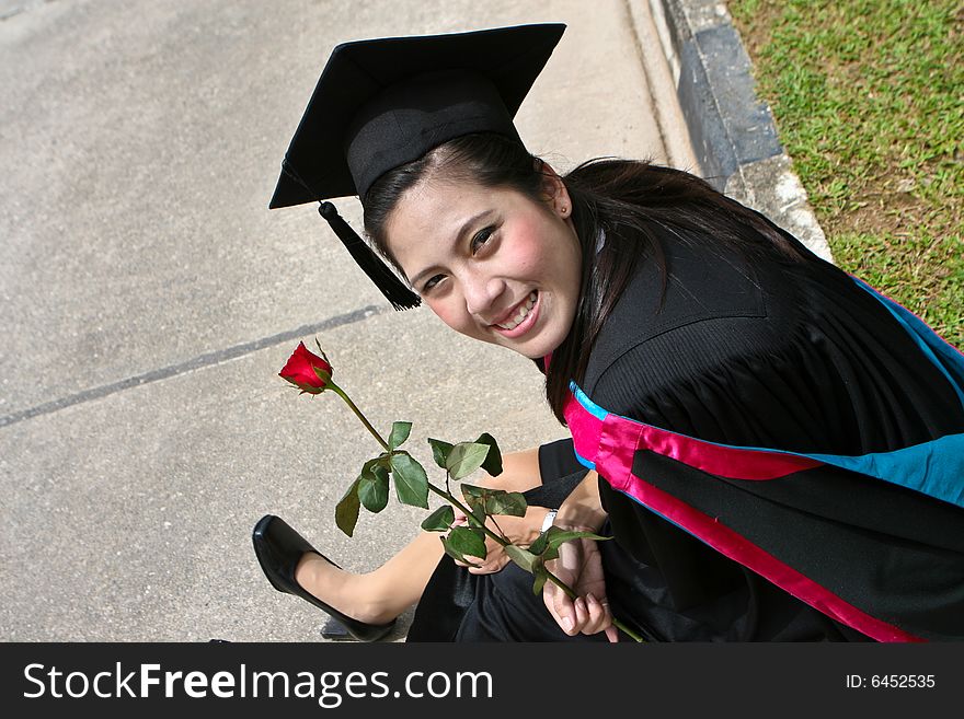 Beautiful Asian university graduate with a red rose.