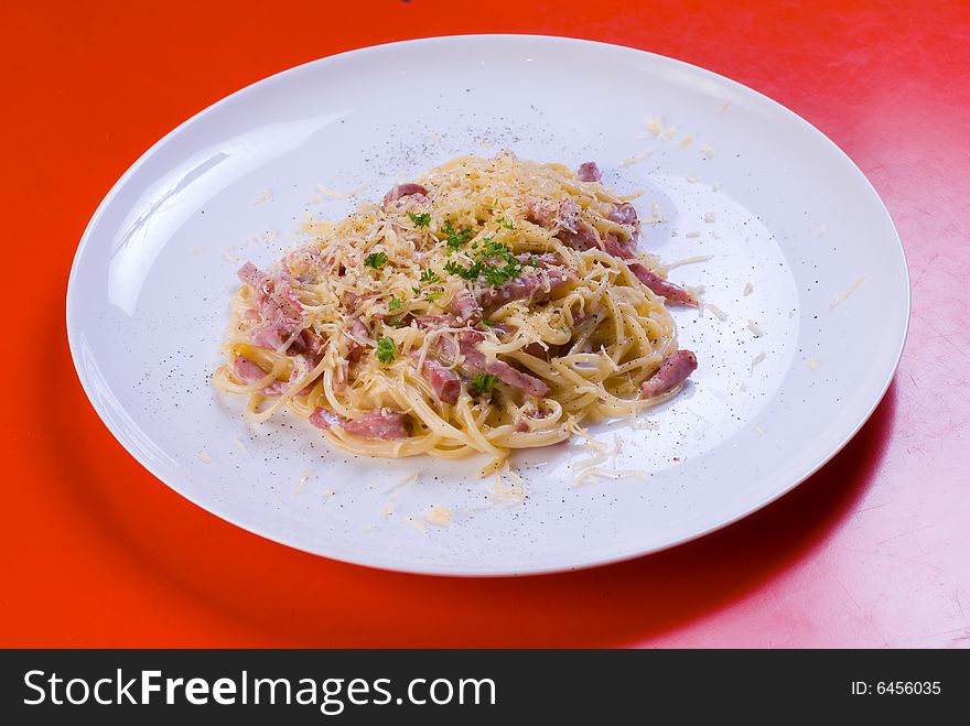 Freshly cooked plate of spaghetti with ham and cheese, decorated with green herbs