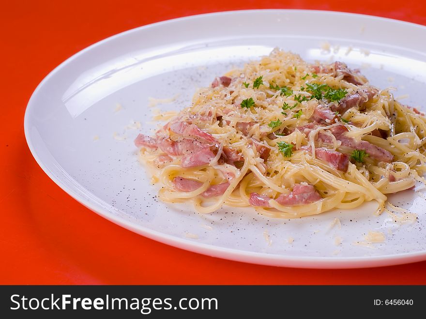 Freshly cooked plate of spaghetti with ham and cheese, decorated with green herbs