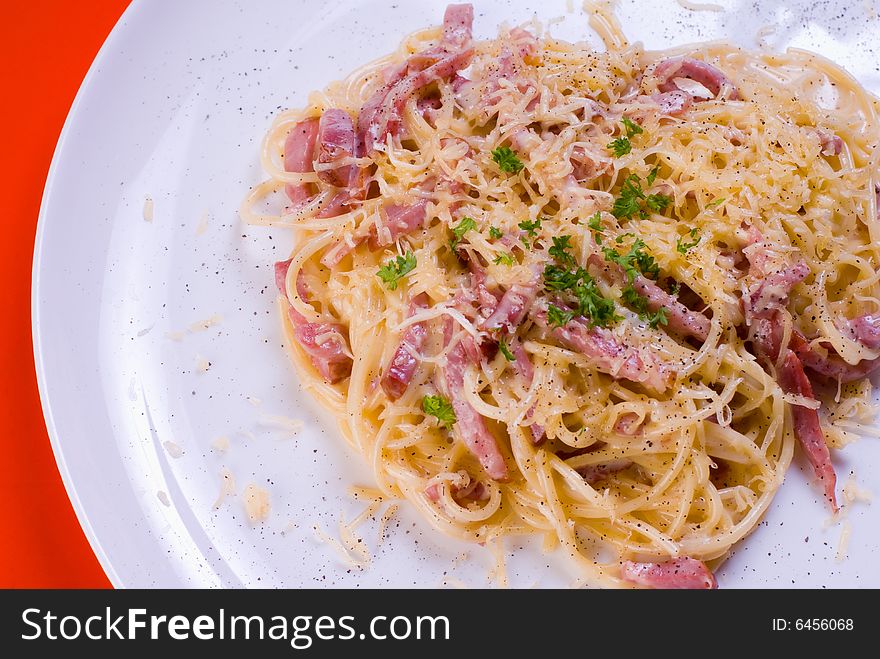 Freshly cooked plate of spaghetti with ham and cheese, decorated with green herbs