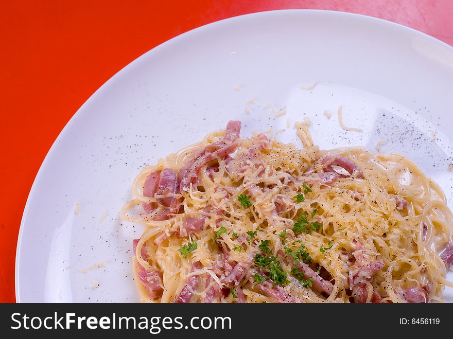 Freshly cooked plate of spaghetti with ham and cheese, decorated with green herbs