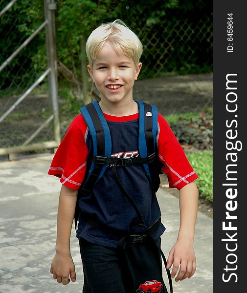 Young boy walks up driveway after school, carrying backpack. Young boy walks up driveway after school, carrying backpack