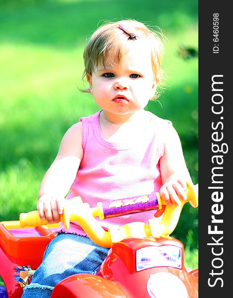 A one year old little girl sits on her toy ATV (All Terrain Vehicle). A one year old little girl sits on her toy ATV (All Terrain Vehicle).