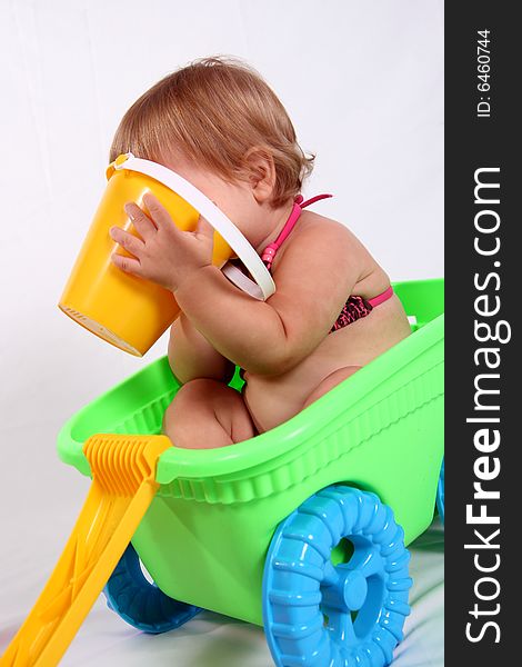 An adorable baby girl sits in a wagon while she plays with her pail. An adorable baby girl sits in a wagon while she plays with her pail.