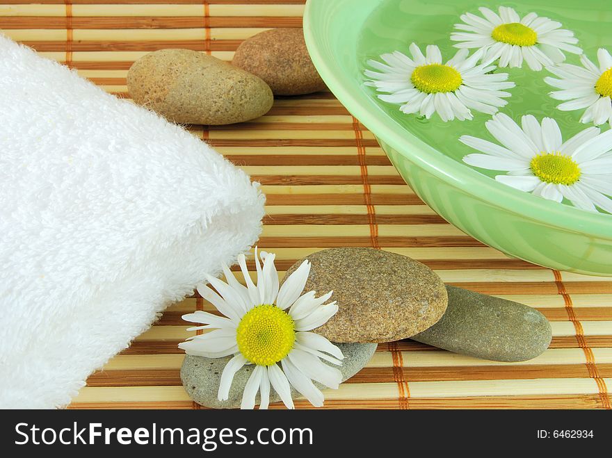 Towel, bowl with daisy and spa stone on the mat