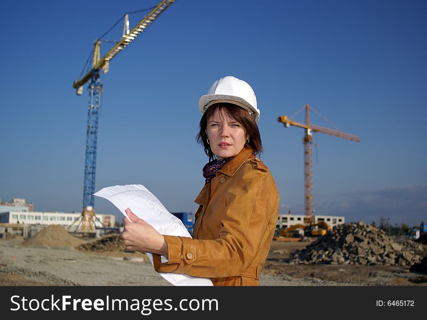 Pretty woman architect holding blueprints and standing in the building site. Pretty woman architect holding blueprints and standing in the building site