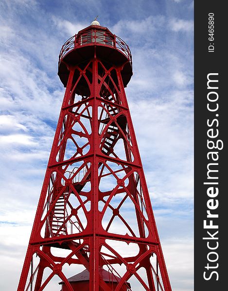 Old red steel lighthouse against a clouded blue sky. Old red steel lighthouse against a clouded blue sky