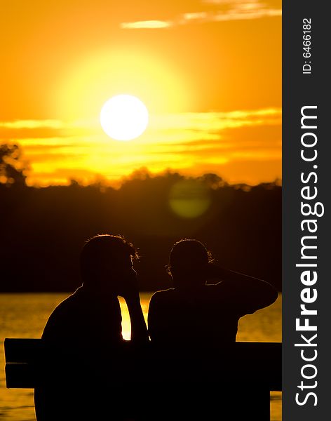 A heterosexual couple on a bench in a public park at sunset. A heterosexual couple on a bench in a public park at sunset