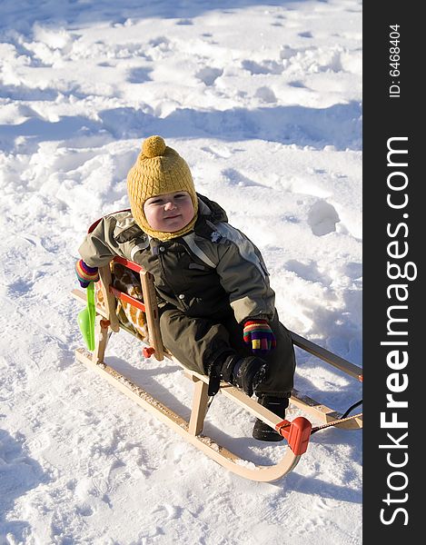 Baby in green coat sitting in sled sled in snow-covered park. Baby in green coat sitting in sled sled in snow-covered park