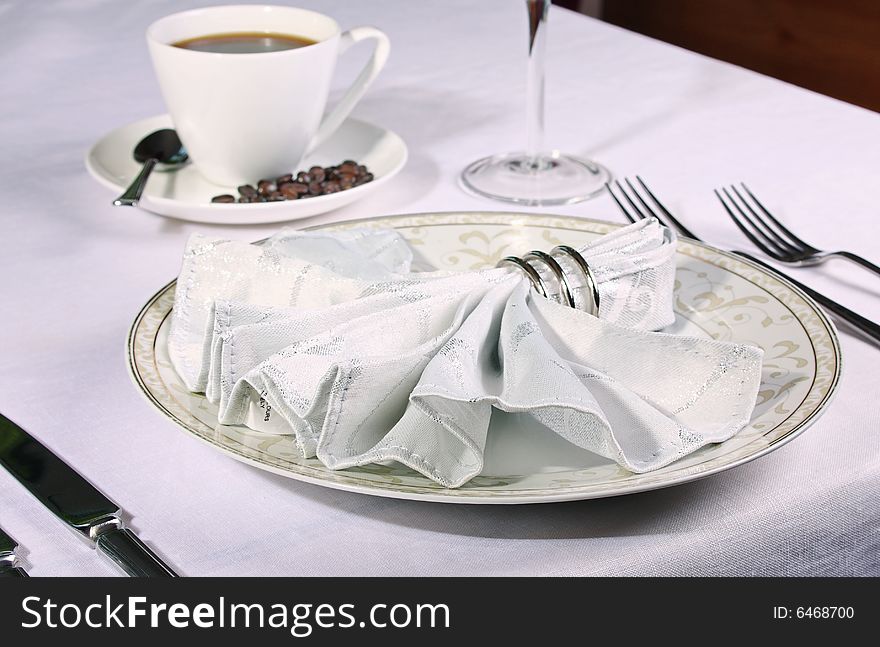 Elegant place setting with piping coffee in background and white fan napkin and ring