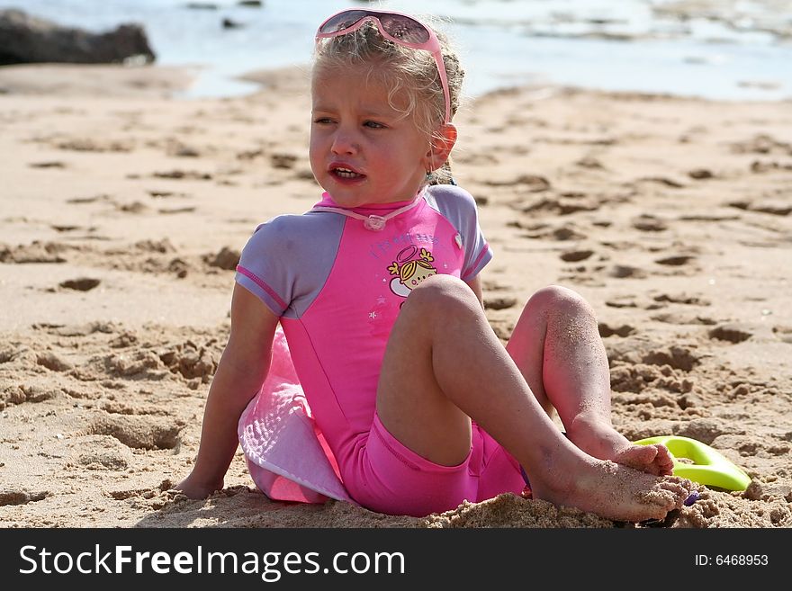 Little girl playing in the sand on the beach with a dirty face wearing sunglasses on her head winking and smiling. Little girl playing in the sand on the beach with a dirty face wearing sunglasses on her head winking and smiling