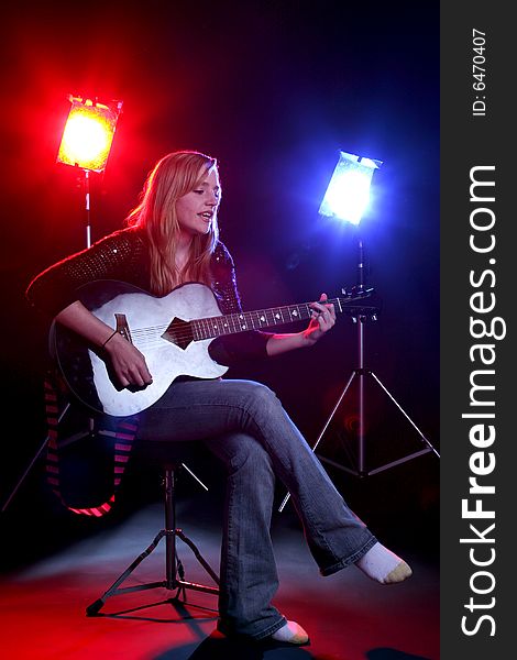 Woman singing and playing guitar on stage with colored concert lights. Woman singing and playing guitar on stage with colored concert lights