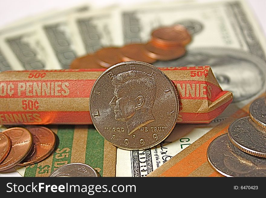 Kennedy half dollar, with pennies, nickels, dimes and quarters, all laid out on money rolls and hundred dollar bills.