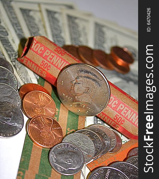 Kennedy half dollar, with pennies, nickels, dimes and quarters, all laid out on money rolls and hundred dollar bills.