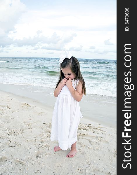 Little girl dressed in white pouting while standing on the beach with the ocean in the background. Little girl dressed in white pouting while standing on the beach with the ocean in the background.