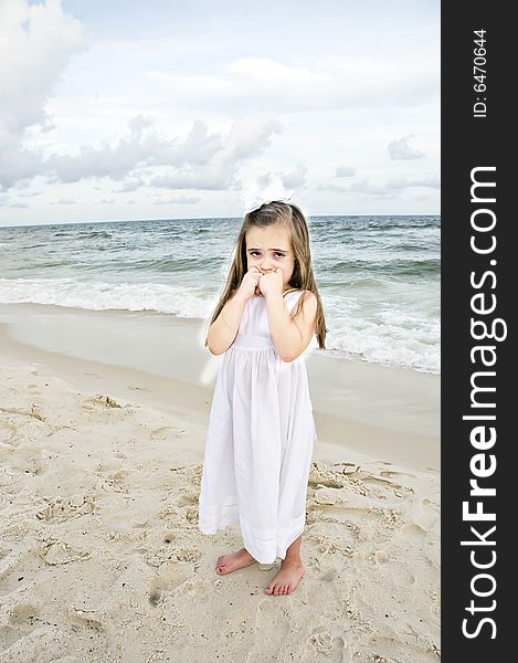 Little girl dressed in white pouting while standing on the beach with the ocean in the background. Little girl dressed in white pouting while standing on the beach with the ocean in the background.