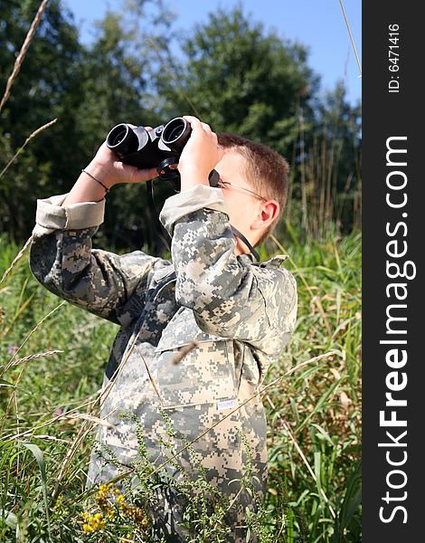 Boy in camouflage looking through binoculars in a field. Boy in camouflage looking through binoculars in a field