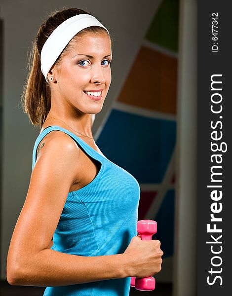 Attractive young woman curling a dumbbell with a happy smile. Attractive young woman curling a dumbbell with a happy smile