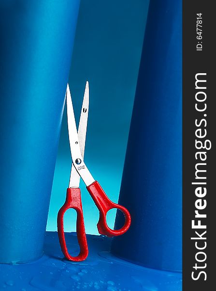 Red scissors stand place on the blue color rolled paper