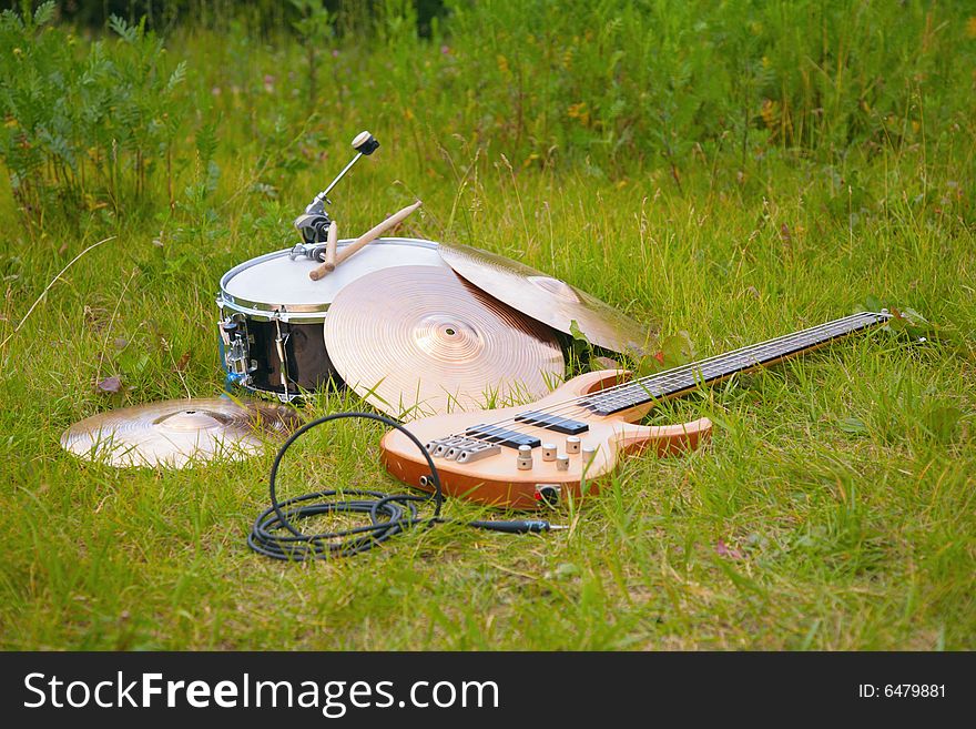 Musical instruments, guitar, drum, plates on green grass.