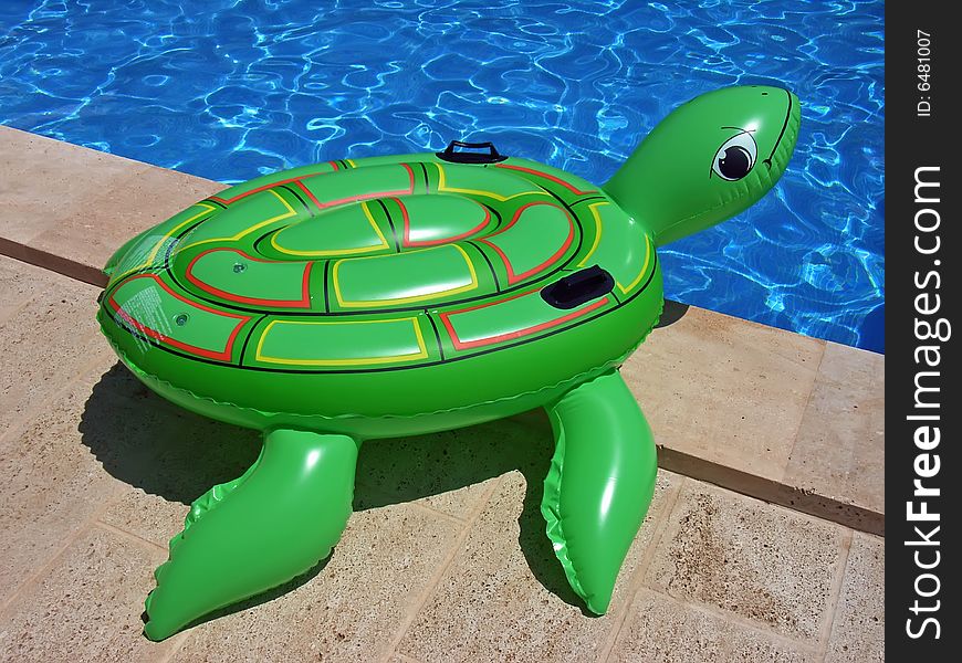 Green inflatable turtle on the edge of a swimming-pool. Green inflatable turtle on the edge of a swimming-pool