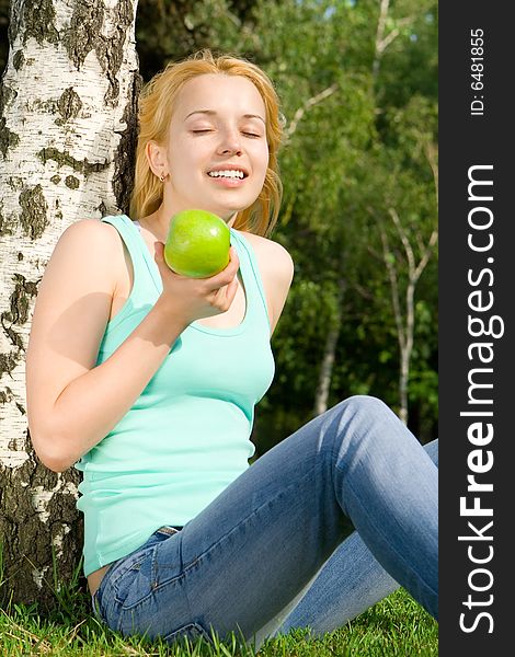 Pretty woman eating green apple on the summer glade