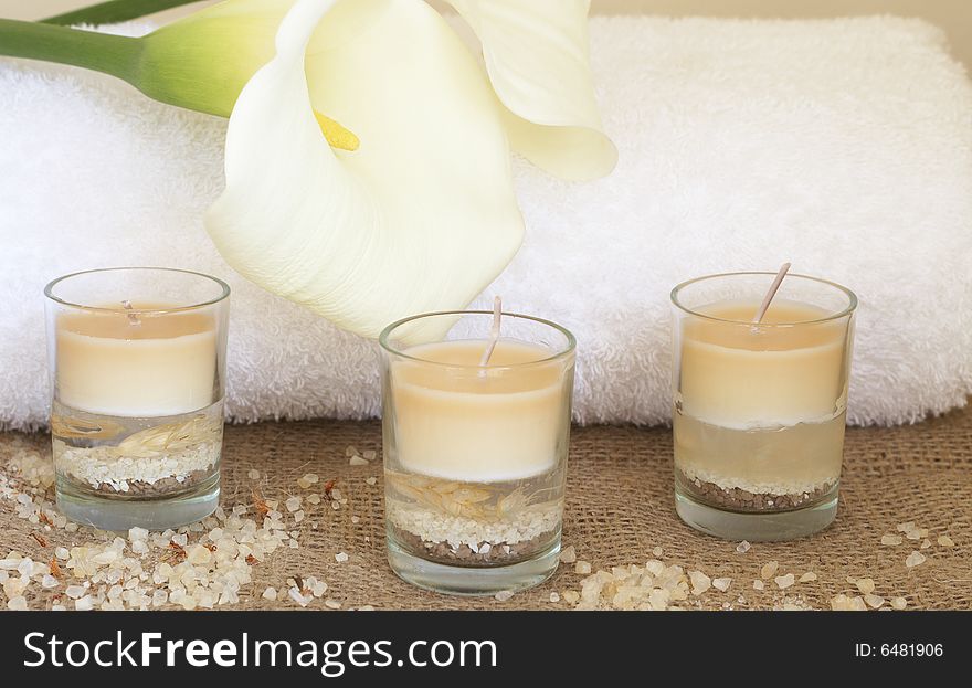 Relaxing spa scene with a white rolled up towel, white lillies, beautiful handmade candles and bath salts