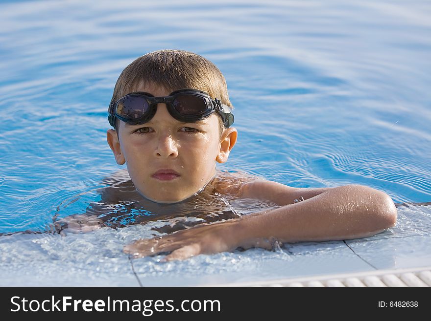 A boy holding in the side of a swimming pool with goggles. A boy holding in the side of a swimming pool with goggles