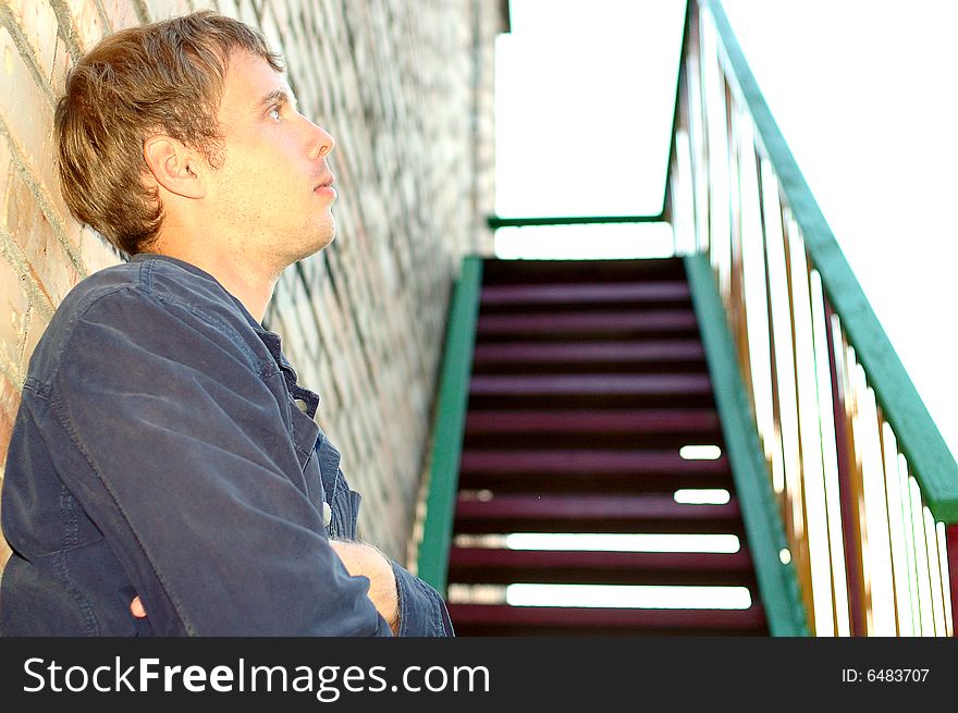 Young stylish man with blonde hair stand near brick wall and stairs. Young stylish man with blonde hair stand near brick wall and stairs.
