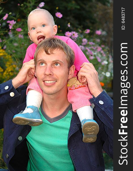 Proud father with his happy daughter sit on father's shoulders on flowers background. Proud father with his happy daughter sit on father's shoulders on flowers background.