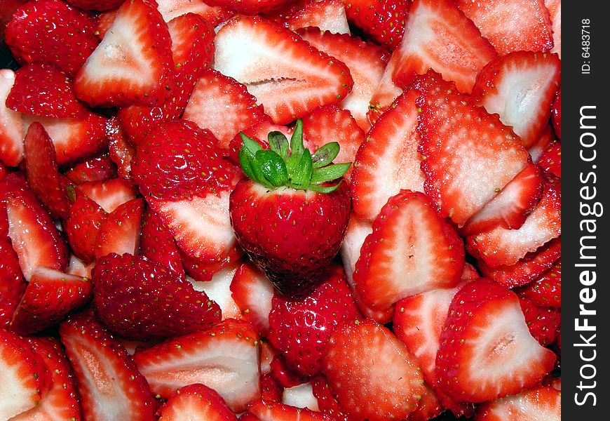 A pile of cut strawberries, with one whole one in the middle.