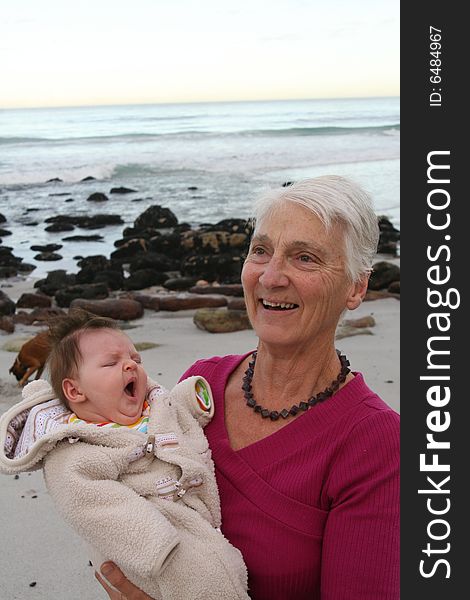 Grandmother with new granddaughter by the sea - family dog in the background. Grandmother with new granddaughter by the sea - family dog in the background