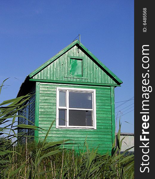 Exterior of green hut or shed in grassy field with blue sky background.