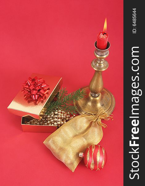 Christmas still life.Christmas candle with flame,present,christmas ball and tree.Red background.