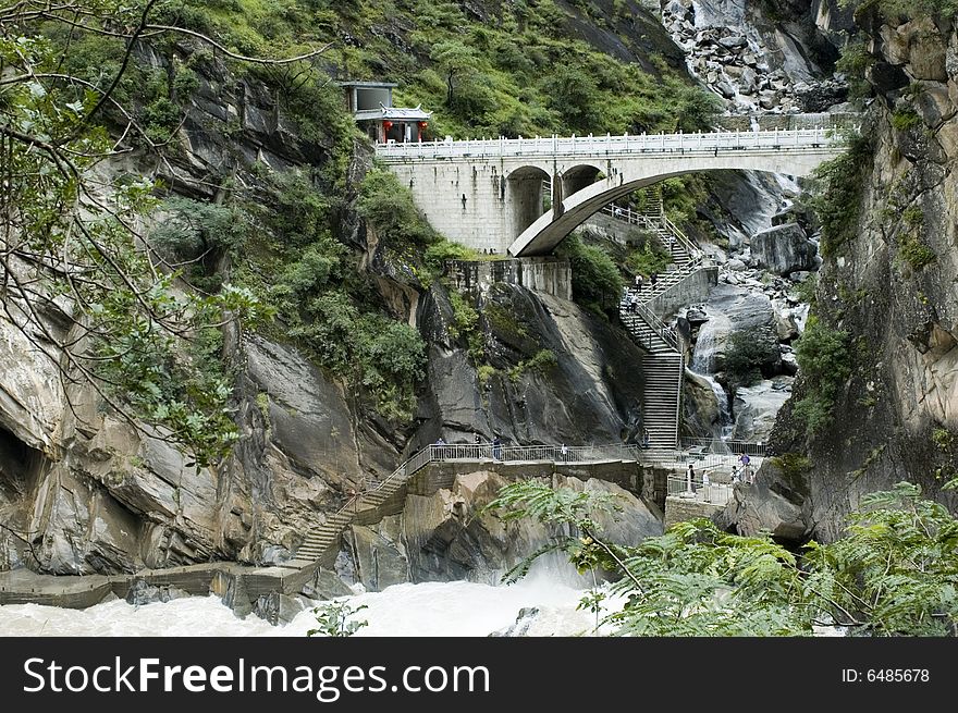 Sino-Tibetan mountains in Yunnan province, near Lijiang city, China. Bridge in ancient Chinese style over river.