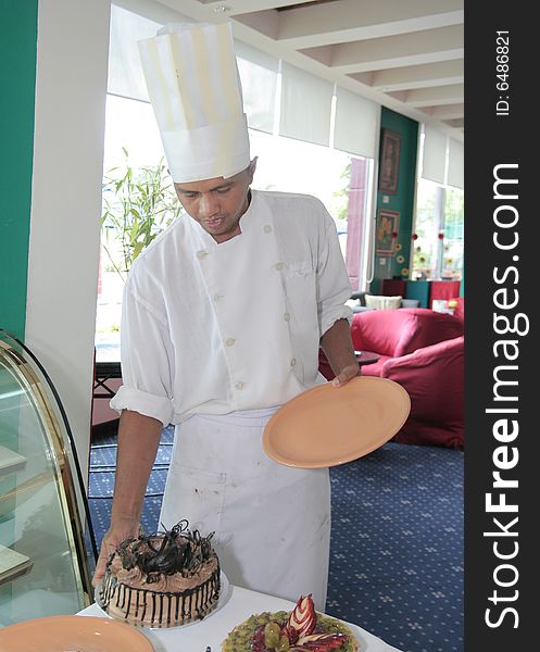 Chef pastry in pose next by cake display