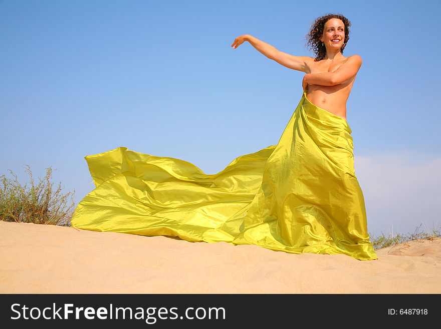 Naked woman with yellow fabric on sand