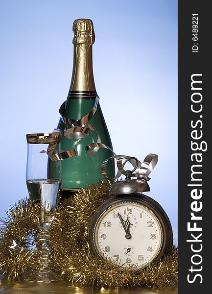 Champagne with glass, old alarm clock and golden decoration on blue