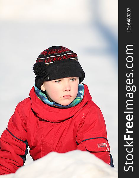 Boy in red snowsuit and hat sitting in a snowbank
