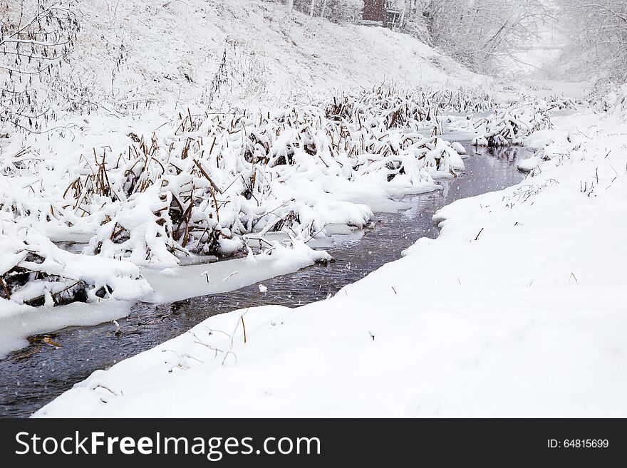 A small river cuts its way through snow covered landscape. It is still snowing and the river is freezing bit by bit. A small river cuts its way through snow covered landscape. It is still snowing and the river is freezing bit by bit.
