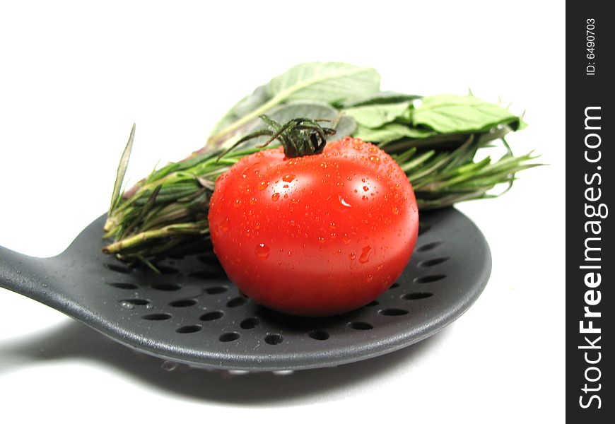 A tomato and some herbs on a spoon. A tomato and some herbs on a spoon