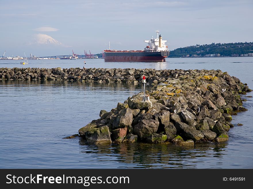 Seascape on Puget Sound of cargo ship and rock jetty, Mount Rainier in distance.