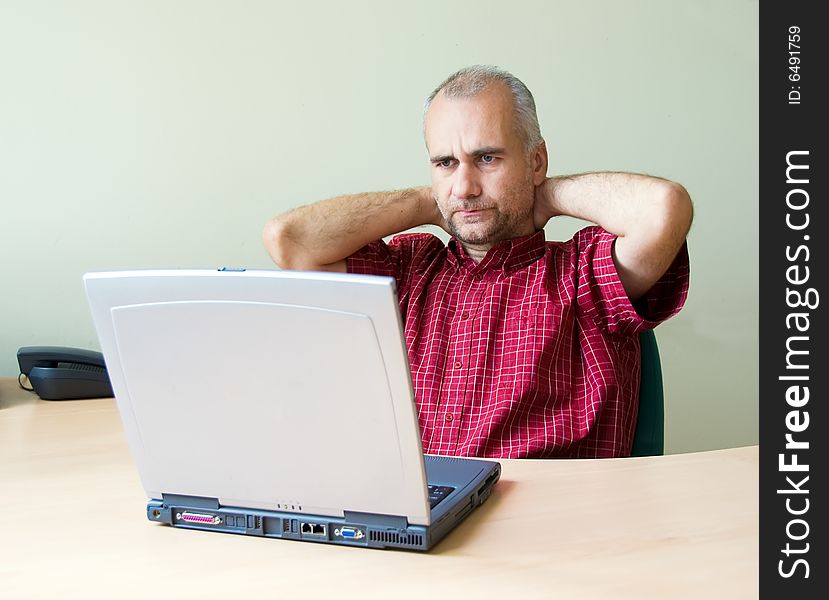 Thoughtful office worker working at the desk with laptop with hands on his neck