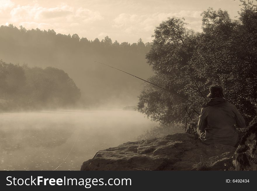 Lonely fisherman sitting on a bank of misty river. Lonely fisherman sitting on a bank of misty river