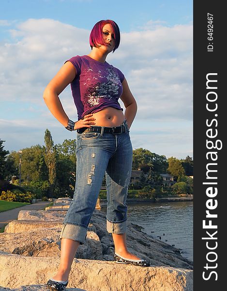 An red hair girl in jeans standing on the shore of lake Ontario at sunset. An red hair girl in jeans standing on the shore of lake Ontario at sunset.