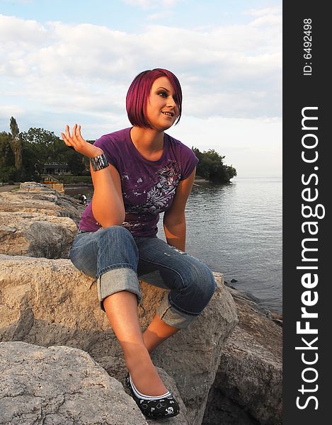 An red hair girl in jeans sitting on the shore of lake Ontario at sunset. An red hair girl in jeans sitting on the shore of lake Ontario at sunset.