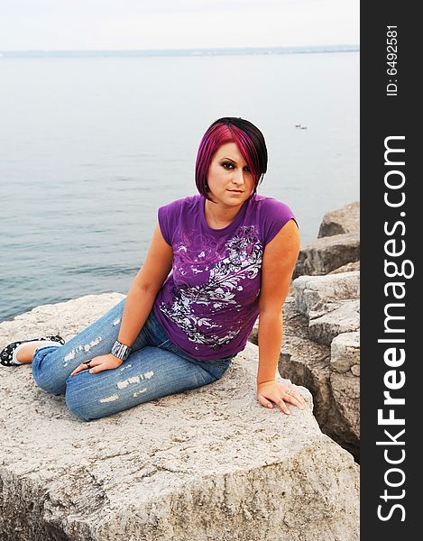 An red hair girl in jeans sitting on the shore of lake Ontario at sunset. An red hair girl in jeans sitting on the shore of lake Ontario at sunset.