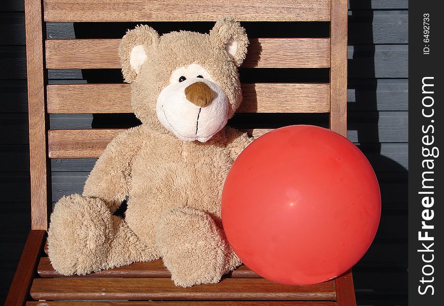 Toy teddy bear holds a red balloon