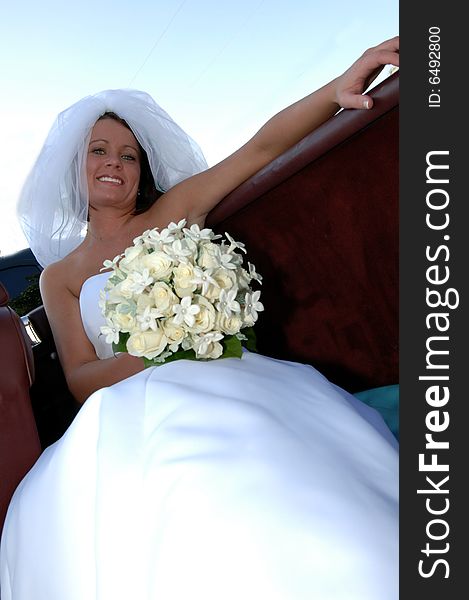 A beautiful smiling bride holding a white rose bouquet sitting in the back seat of a convertible. A beautiful smiling bride holding a white rose bouquet sitting in the back seat of a convertible