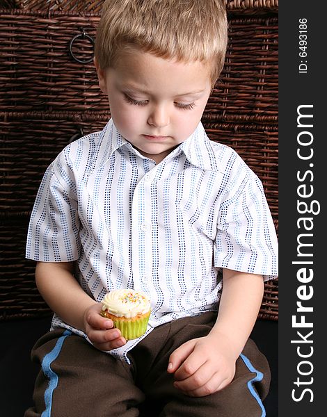 Beuatiful Blond toddler looking down at his cupcake. Beuatiful Blond toddler looking down at his cupcake